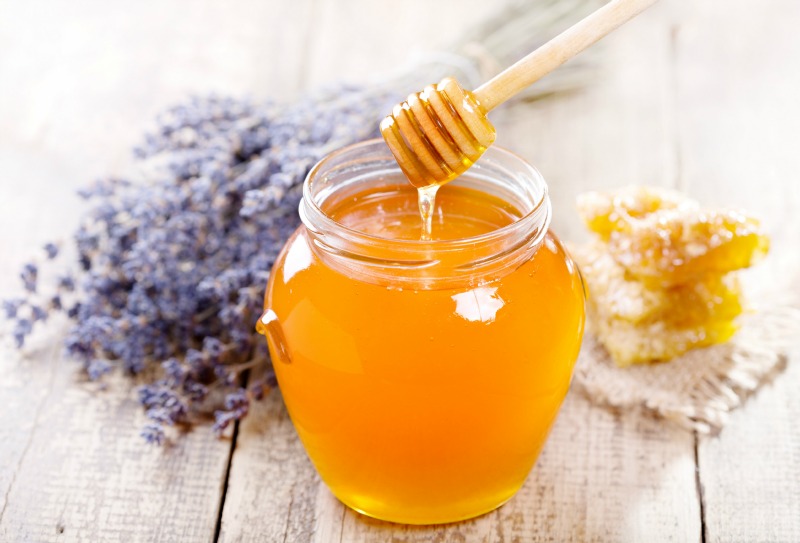 jar of honey with honeycomb and lavander flowers on wooden table