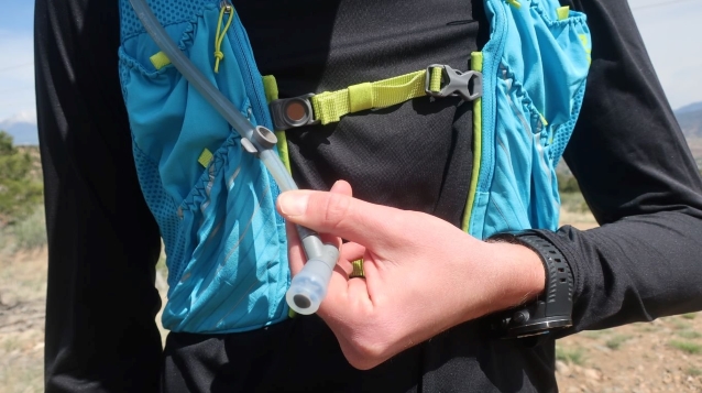 A person holding the drinking hose from a hydration pack worn on their back.